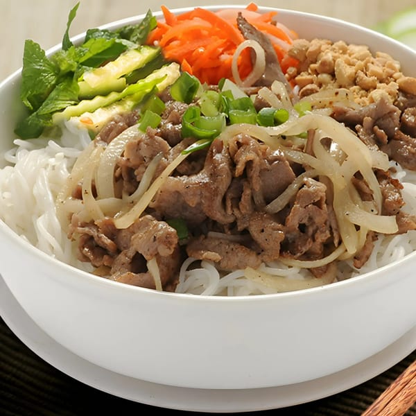 A white bowl of BMC Pho's Vietnamese vermicelli noodles with beef, onions, carrots, and peanuts.