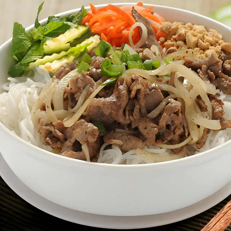 A white bowl of BMC Pho's Vietnamese vermicelli noodles with beef, onions, carrots, and peanuts.