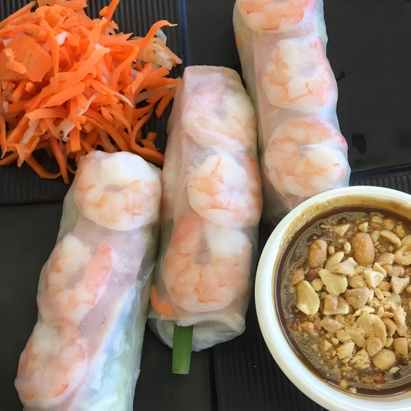 Three Vietnamese shrimp spring rolls with shredded carrots and a bowl of peanut dipping sauce.