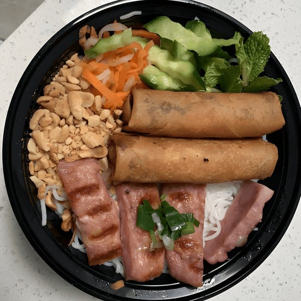 A Vietnamese vermicelli bowl with grilled pork, spring rolls, peanuts, and vegetables in a black bowl.