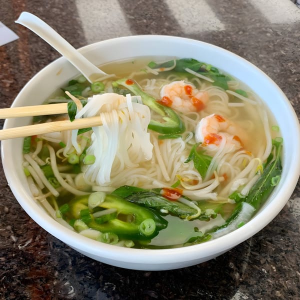 Chopsticks lifting noodles from a bowl of BMC Pho with shrimp, jalapeños, and herbs.