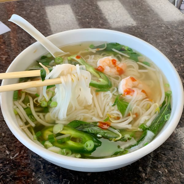 Chopsticks lifting noodles from a bowl of BMC Pho with shrimp, jalapeños, and herbs.
