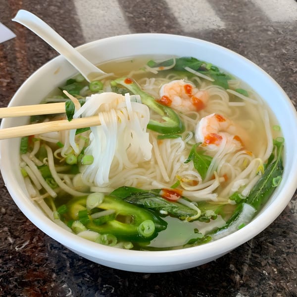 Chopsticks lifting noodles from a bowl of BMC Pho with shrimp, jalapeños, and herbs.