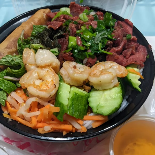 A Vietnamese vermicelli bowl with shrimp, beef, spring roll, and fresh vegetables.