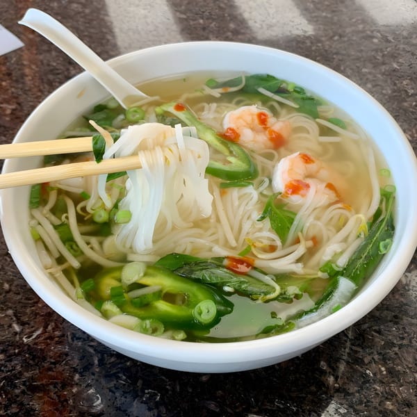 Chopsticks lifting noodles from a bowl of BMC Pho with shrimp, jalapeños, and bean sprouts.